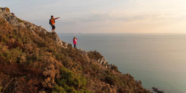 Two hikers admire the Bay of Mont Saint-Michel from the cliffs of Carolles and Champeaux