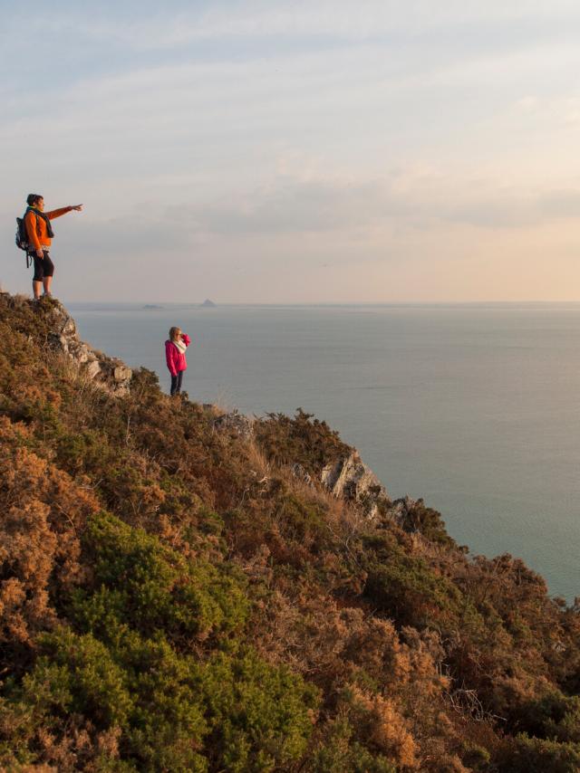 Two hikers admire the Bay of Mont Saint-Michel from the cliffs of Carolles and Champeaux