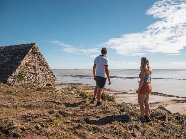 A couple observes Tombelaine and Mont saint-Michel from the Vauban hut on the Champeaux cliffs