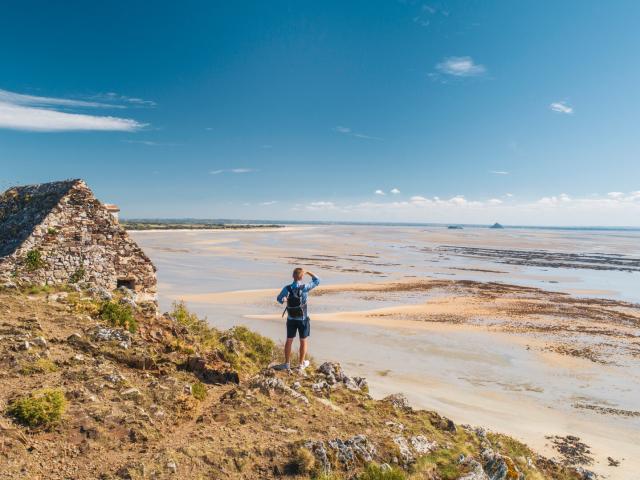 Un randonneur observe la baie du Mont Saint-Michel depuis la cabane Vauban sur les falaises de Champeaux