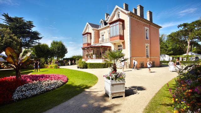 Des visiteurs se promènent sous un beau ciel bleu dans le jardin Christian Dior à Granville tout autour du musée dédié au célèbre couturier