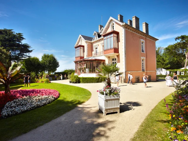 Des visiteurs se promènent sous un beau ciel bleu dans le jardin Christian Dior à Granville tout autour du musée dédié au célèbre couturier