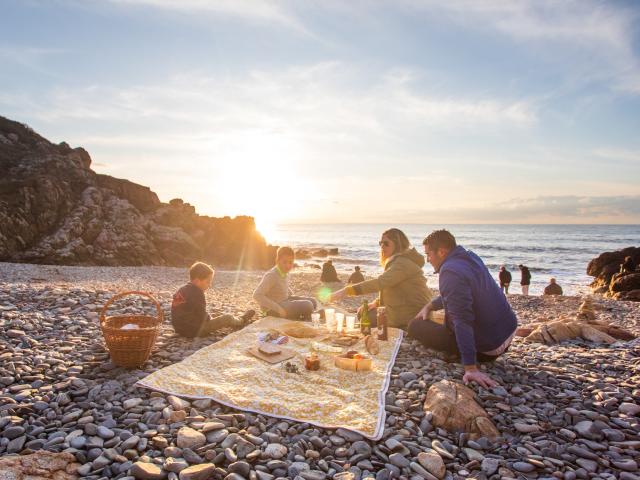 Une famille pique-nique sur les galets du port du Lude au coucher du soleil